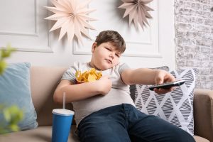 Overweight,boy,watching,tv,with,snacks,indoors