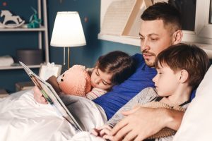 Father,reading,bedtime,story,to,his,little,children,at,home